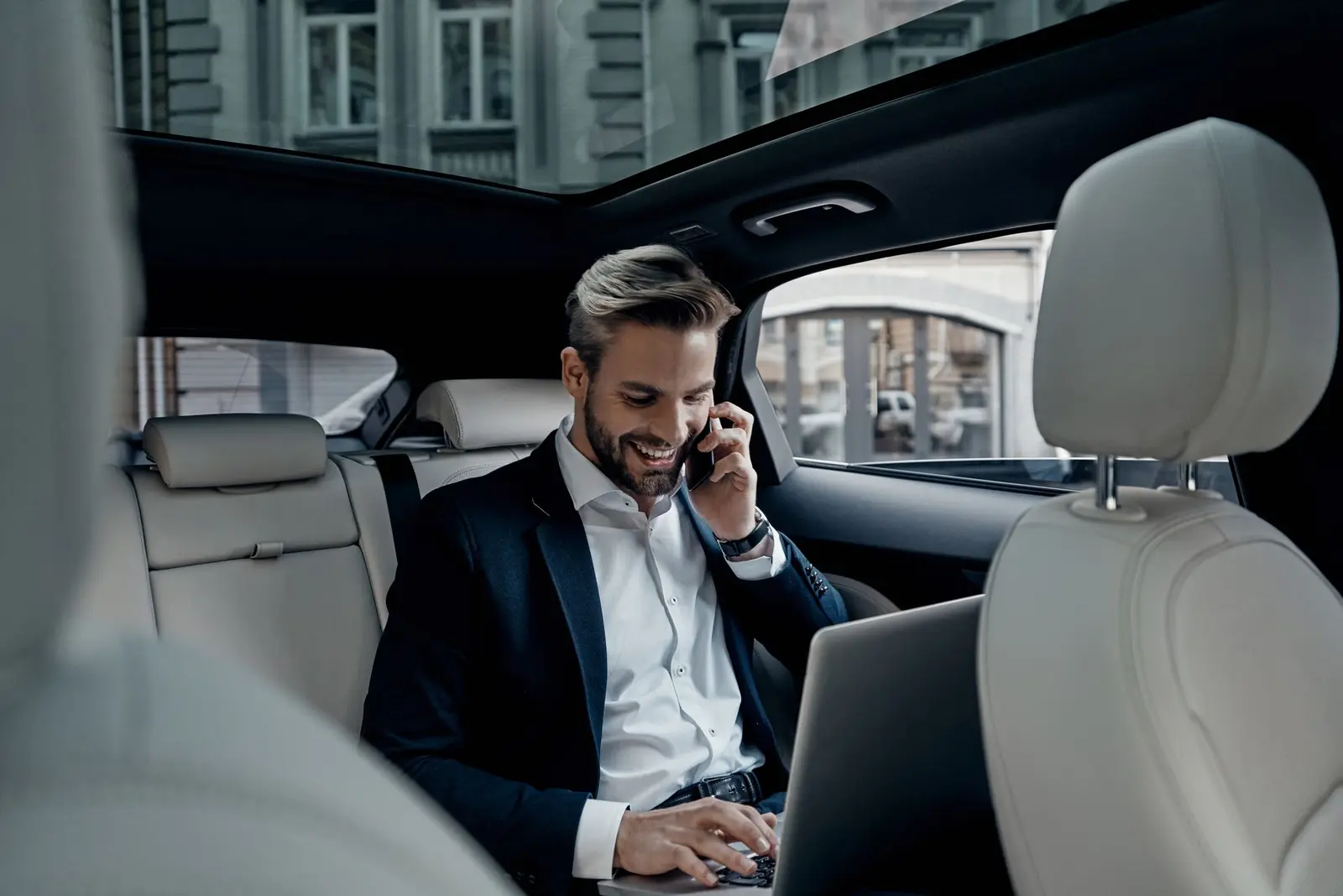 Executive working on a laptop and phone in the back seat of a chauffeured black car in Chicago